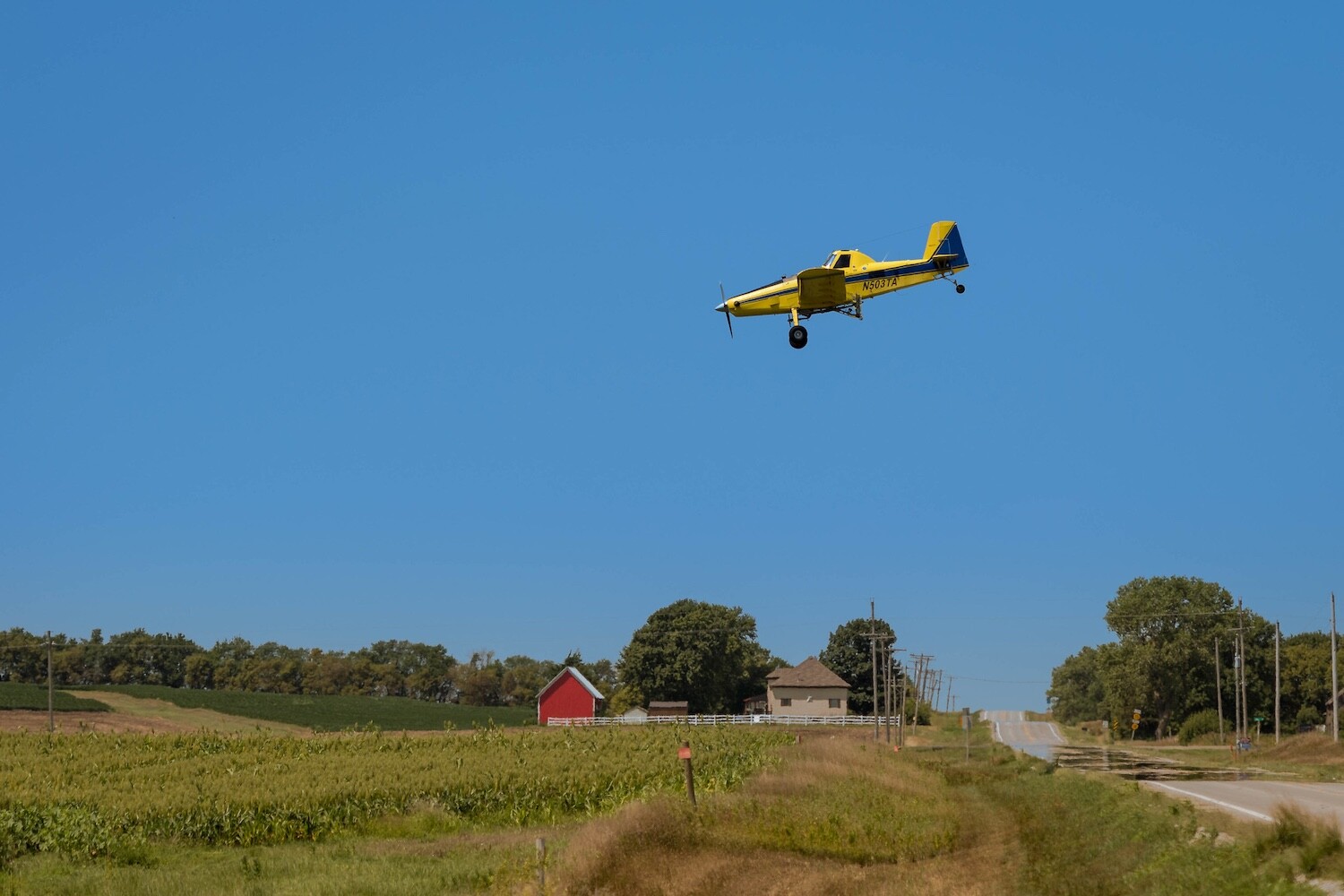 Lightroom Object Selection, a yellow airplane flying low over a field.